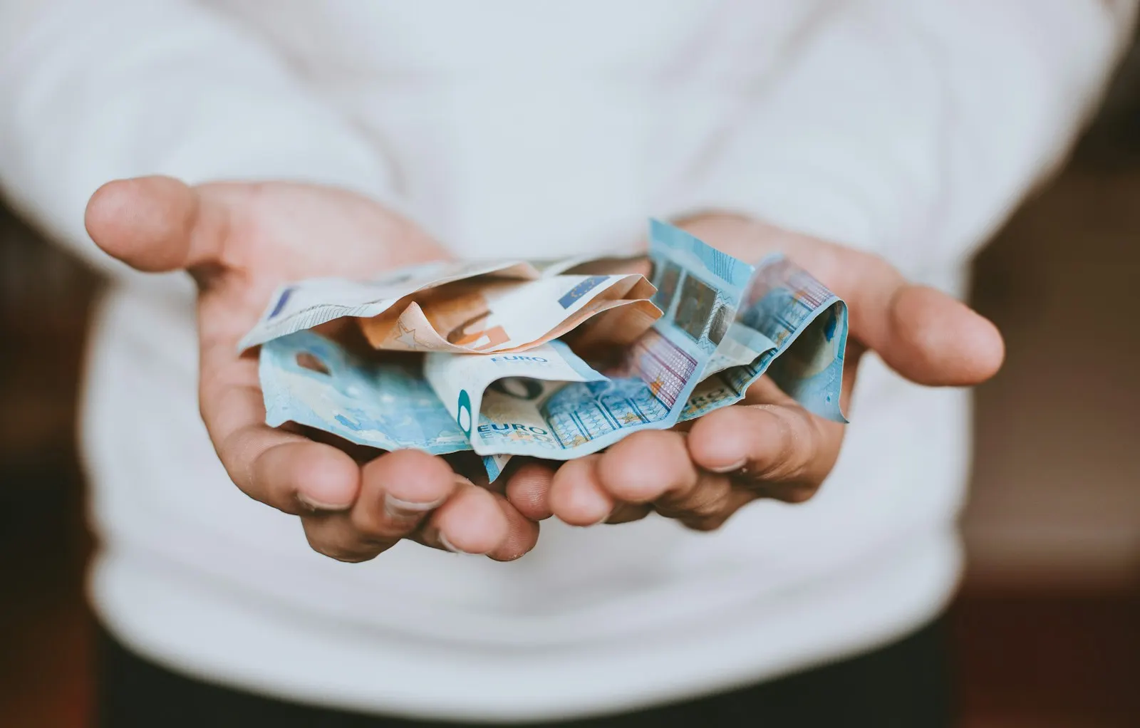 Deux mains ouvertes tiennent quelques billets en euros froissés