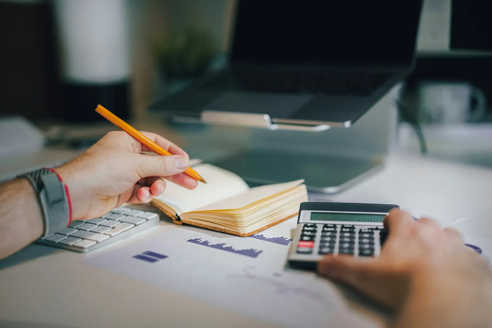 Des mains tiennent un crayon et une calculatrice au-dessus d'un carnet ouvert