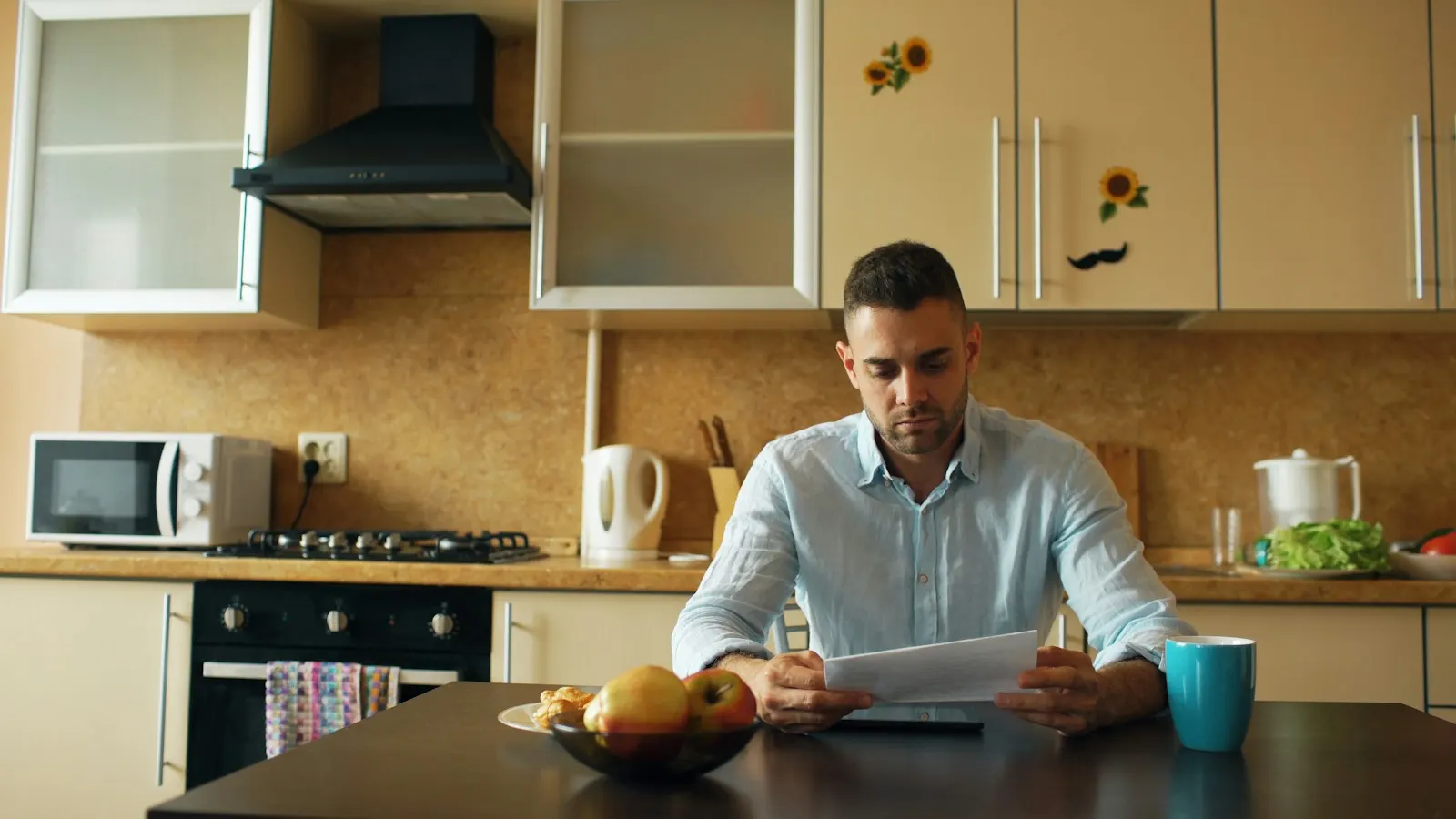 Un homme lit un courrier à la table de sa cuisine, l'air préoccupé