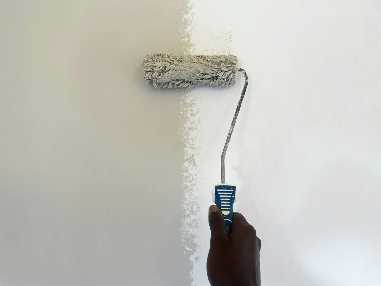 Une main passe un rouleau de peinture blanche sur un mur intérieur