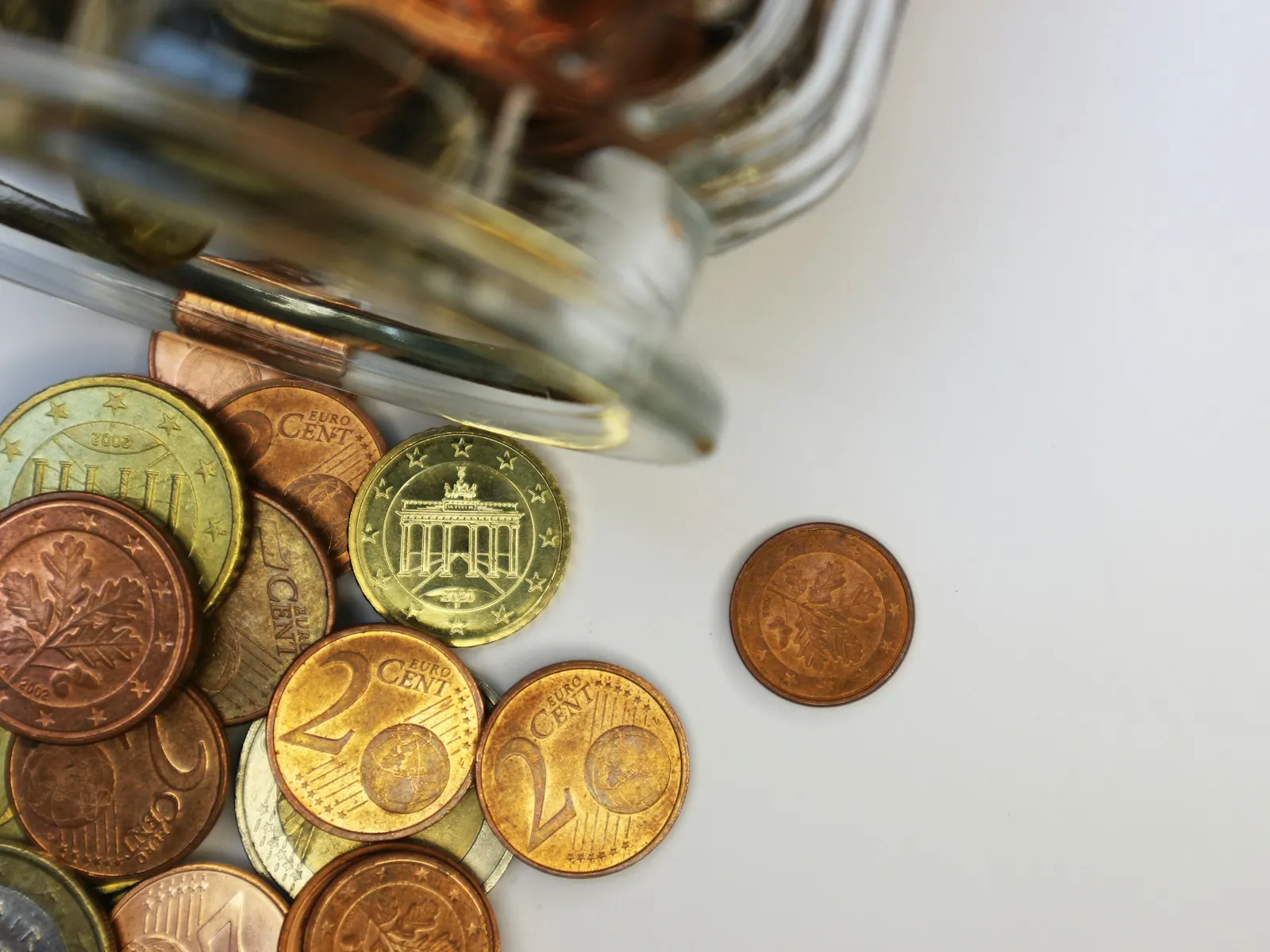 Pièces en euros et centimes renversées d'un bocal en verre sur fond blanc