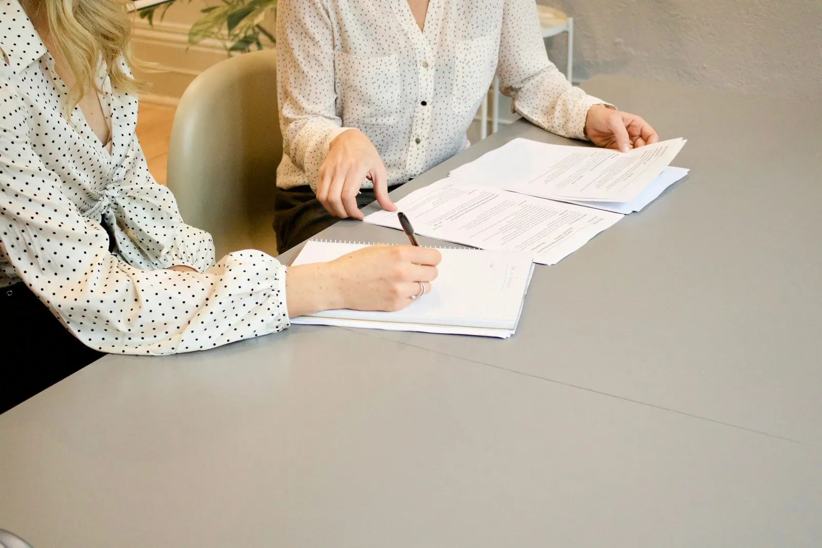 Deux femmes assises à une table, l'une signe un document au stylo