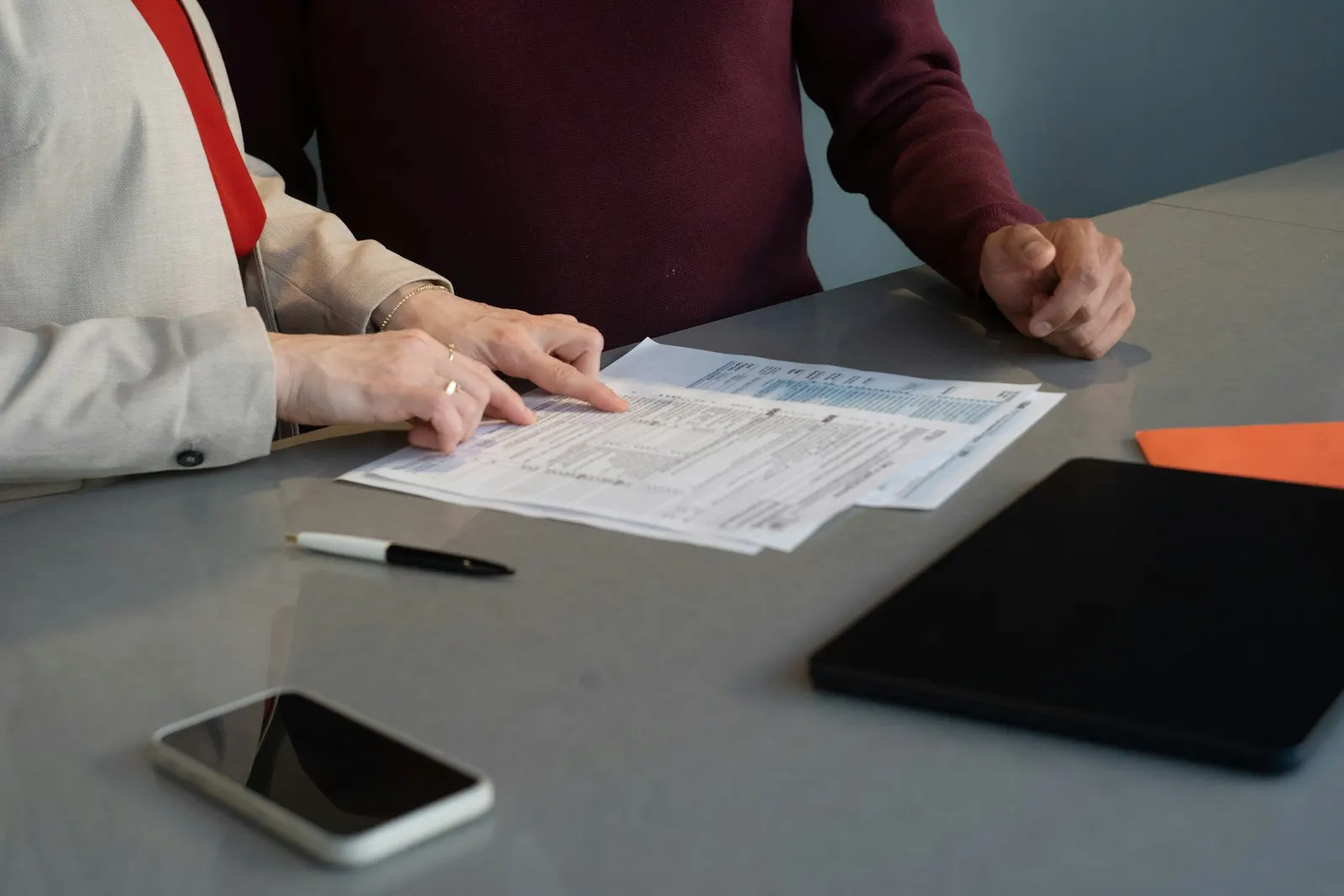 Deux personnes relisent ensemble un document posé sur une table grise, un stylo à côté